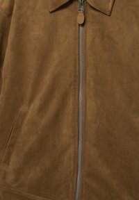 Hnedá semišová bunda so strieborným kovovým zipsom, špicatým golierom a dvoma prednými vreckami s lemom.