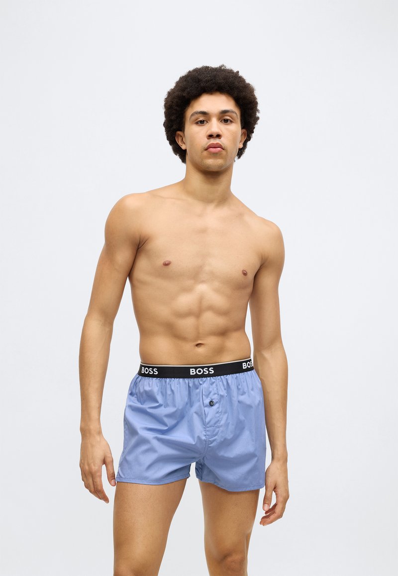 Lyseblå boxershorts laget av mykt stoff, med svart midjebånd med "BOSS"-logo og knappeåpning foran.