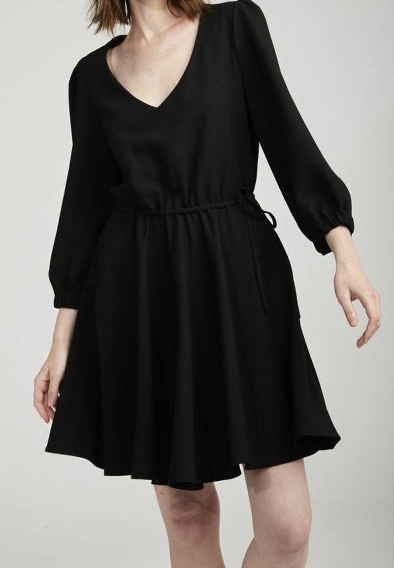 Svart A-linje klänning med djup V-hals, långa puffärmar och justerbart midjeband. Tillverkad av mjukt tyg, har den två sidofickor.