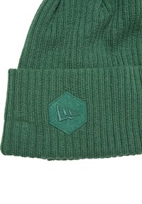 Berretto di maglia verde con una texture a costine. Presenta un patch esagonale con un logo in rilievo di una tonalità di verde leggermente più scura.