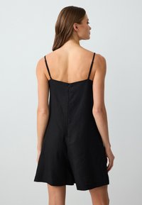 Rompers en lin noir avec de fines bretelles ajustables, un dos droit, une fermeture à glissière et une coupe décontractée. Tissu texturé avec une finition mate.