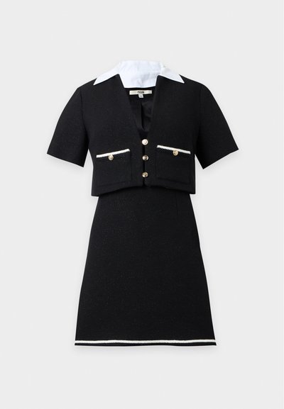 Robe noire à manches courtes avec veste courte boutonnée, col blanc, poches avant et bordure blanche le long de l'ourlet de la jupe.