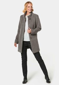 Gray wool blend coat with a high collar, featuring three buttons, side pockets, and a relaxed fit. Worn over a white top and black pants.