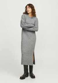 Pilkos megztos suknelės ilgomis rankovėmis ir šoninėmis plyšiais, su raukinėtu kraštu. Suderinta su juodais iki kelių batais kontrastui.