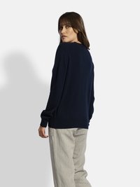 Granatowy sweter robiony na drutach z okrągłym dekoltem, długimi rękawami i luźnym krojem. Pasek w paski dopełnia outfit.