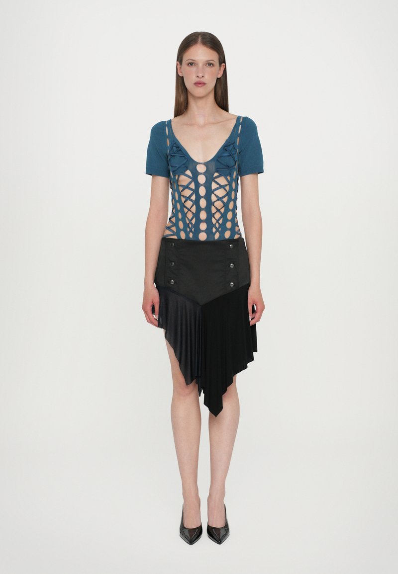 Blue cut-out bodysuit with circular openings, paired with a black asymmetrical pleated skirt featuring buttons and smooth texture. Black heels.