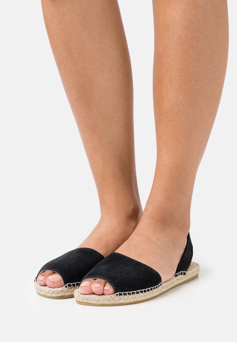 Svart mocka espadrille-lägenheter med öppen tå, en vävd jutesula och sömnadsdetaljer. Slät textur, minimalistisk design och låg profil.