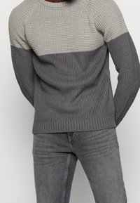 Stickad tröja med färgblockeringsdesign i ljusgrått och mörkgrått. Har rund halsringning, ribbad nederkant och texturerade detaljer.