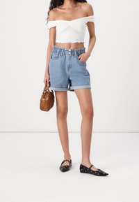 Ljusblå denimshorts med uppvikta ärmar och ett gathered midjeband. Vit off-shoulder crop top. Svarta lägenheter med öljettackcenter, brun handväska.