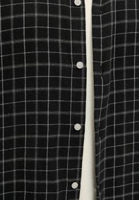 Must-valgete ruuduline särk, mille nööbid on osaliselt lahti, paljastades valge sisemuse.