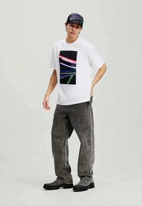 Λευκό γραφικό t-shirt με ορθογώνια μαύρη εκτύπωση με πολύχρωμες γραμμές, σε συνδυασμό με ξεθωριασμένο γκρι τζιν παντελόνι και μαύρες φλατ εσπαντρίγιες.