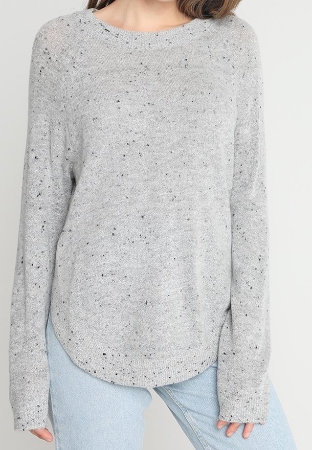 Grauer Strickpullover mit schwarzen Sprenkeln, runder Halslinie, langen Ärmeln und abgerundetem Saum, kombiniert mit hellblauen Jeans.