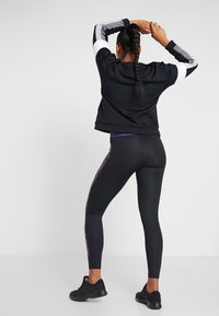 Czarny sportowy sweatshirt z białymi i szarymi paskowanymi rękawami, zestawiony z czarnymi legginsami z fioletowym bocznym paskiem i teksturowanymi akcentami.