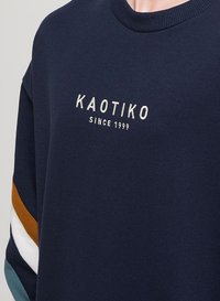 Marine sweatshirt lavet af blødt stof med rund hals. Har hvidt broderet logo "KAOTIKO SINCE 1999" og farvestribede ærmer.