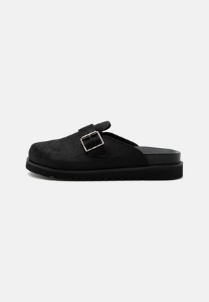 Schwarzer Slip-On-Clog mit strukturierter Oberseite, silbernem Schnallenriemen und dicker geriffelter Sohle, seitlich auf weißem Hintergrund dargestellt.