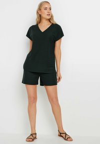 Top verde oscuro con cuello en V y mangas cortas, combinado con pantalones cortos a juego. Tejido suave con un ajuste relajado, sin patrones o adornos visibles.