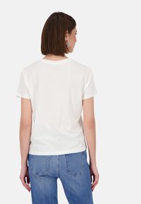 Weißes Baumwoll-T-Shirt mit kurzen Ärmeln, Rundhalsausschnitt und lockerer Passform, kombiniert mit blauen Denim-Jeans mit Gesäßtaschen und geradem Schnitt.