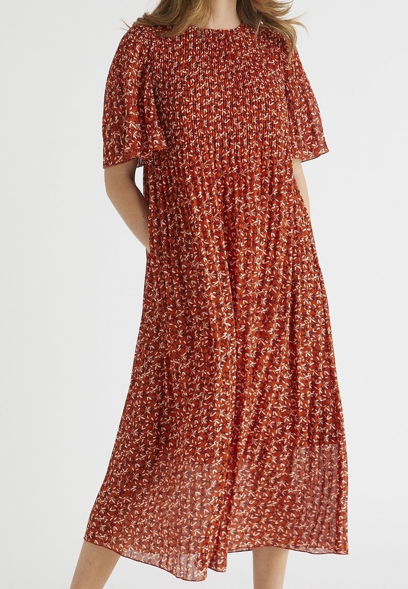 Rode bloemen midi-jurk van lichte stof. Heeft smockwerk bij de halslijn, korte pofmouwen en een vloeiende, geplooide rok.
