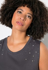 Top a canotta grigio scuro con decorazioni in strass rotondi sul davanti, realizzato in un tessuto morbido, con scollatura rotonda e design senza maniche.