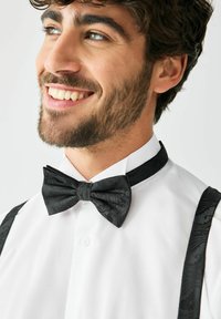 Must mustriga kikilips ja sobivad rihmad, kantud valge kleidisärgiga. Kangal on peened mustrid. Lähedalt portree.