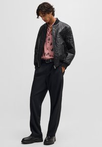 Black bomber jacket with embossed texture, pink patterned shirt beneath, black trousers, and chunky black shoes. Simple design with contrasting colors.