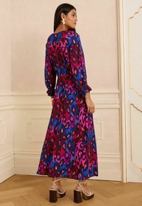 Maxikleid in lebhaftem Rot, Pink und blauem Leopardenmuster. Lange Ärmel mit gerafften Manschetten, tailliertem Schnitt und fließendem Saum.