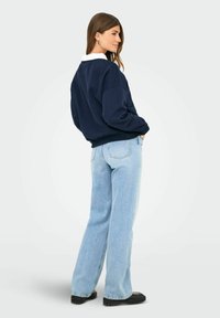 Sweatshirt navy oversized con colletto bianco, abbinato a jeans a gamba larga blu chiaro e stivali platform neri. Tessuto morbido, vestibilità rilassata.