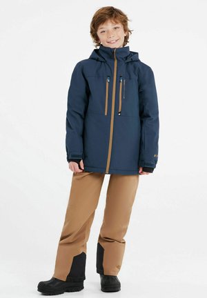 Veste imperméable bleu marine avec zips et accents beige, dotée d'une capuche, de deux poches avant et de poignets ajustables. Pantalon de neige beige avec des finitions noires.