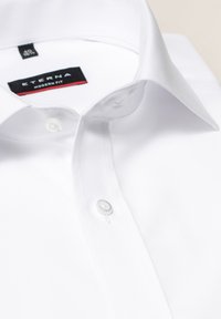 Weiße ETERNA Hemdbluse in modernem Schnitt mit klassischem Kragen, zwei Knöpfen und glatter Stofftextur. Einfaches und sauberes Design.
