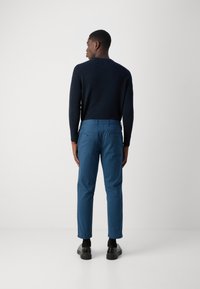 Kék pamut nadrág, normál fazonban, két hátsó zsebbel. Sötét tengerészkék textúrájú pulóverrel és fekete cipővel párosítva.