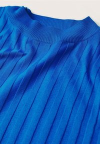 Tissu tricoté côtelé bleu avec des lignes texturées verticales et un col rond, posé à plat sur un fond clair.