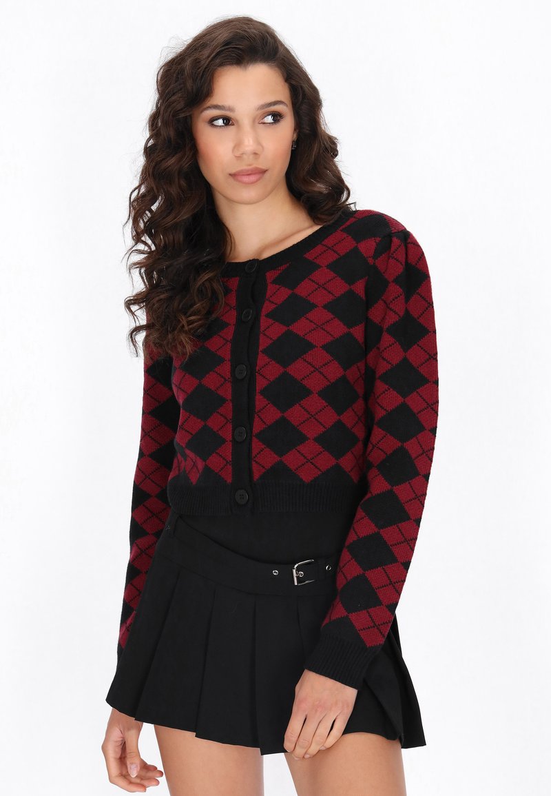 Sarkans un melns argyle raksta īss džemperis ar pogām, ribinātām piedurknēm un gludu tekstūru, kombinēts ar melnu plisētu svārku.
