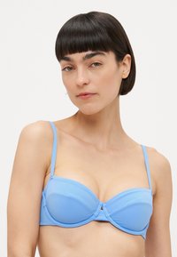 Lys blå bh-top med underwire, tynne justerbare stropper og formede kopper med en sentervridningsdetalj. Glatt, elastisk stoff.
