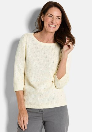 Maglione lavorato a maglia di colore crema chiaro con un motivo testurizzato, ampia scollatura rotonda e maniche a tre quarti. Orlo e polsini a coste, tessuto morbido.