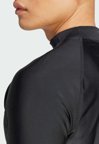 Zwarte sporttop met een hoge kraag, gladde textuur en naden, die een aansluitend ontwerp rond het bovenlichaam laat zien.