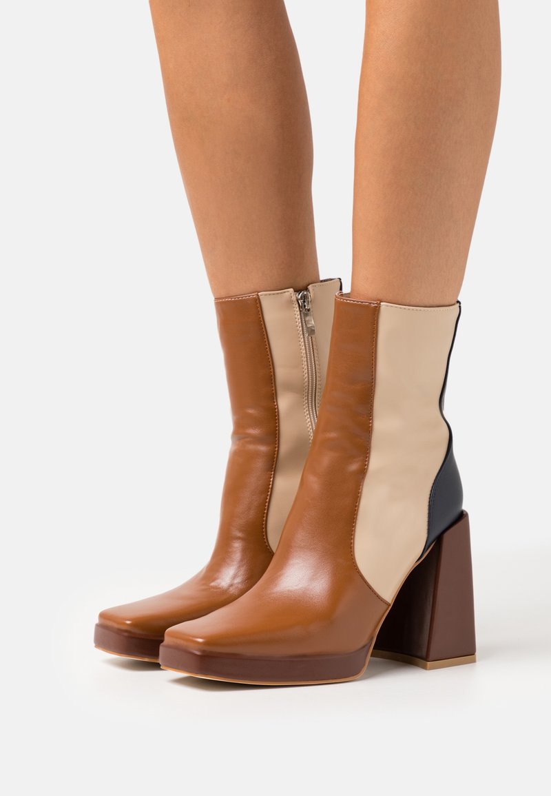 Bottines à talons blocs en blocs de couleurs marron, beige et noir portées sur des jambes nues.