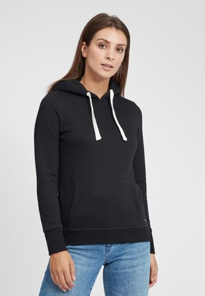 Black hooded sweatshirt made of soft material, featuring white drawstrings, a front pocket, and ribbed cuffs. Styled with blue jeans.