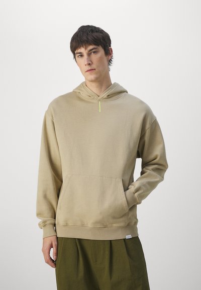 Beige színű kapucnis pulóver, puha anyagból készült, elülső zsebével, bordázott mandzsettákkal és neon zöld részlettel a nyaknál.
