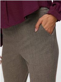 Roku roka novietota pelēko biksu priekšējā kabatā, kopā ar garām piedurknēm maroon krāsas augšdaļu ar savākumiem pie piedurknēm.