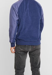 Mörkblå sweatshirt med mjuk textur, utrustad med raglanärmar i en ljusare nyans. Komplett med ribbad fåll och muddar.