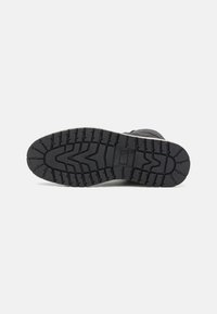 Suela de zapato de goma negra con patrones de surcos profundos y superficie texturizada, diseñada para ofrecer tracción y durabilidad. Bordes reforzados visibles.