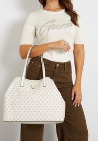 Biała torba na ramię z kremowymi skórzanymi wykończeniami, z geometrycznym wzorem liści i złotymi detalami. Duża torba typu tote z podwójnymi uchwytami.