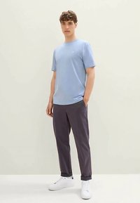 Světle modré tričko s krátkými rukávy a kulatým výstřihem, doplněné tmavě šedými kalhotami a bílými teniskami. Jednoduchý design, bavlněná textura.