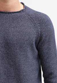 Marinblå stickad tröja med rund hals, strukturerad väv och raglanärmar. Subtila ljusa fläckar överallt förbättrar designen.