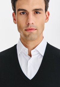 Czarny sweter z dekoltem w serek nałożony na białą koszulę z kołnierzykiem. Sweter ma gładką teksturę i klasyczny krój, prezentując elegancki wygląd.