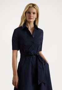 Navy blue shirt dress made of cotton, featuring a collared neck, short sleeves, a tied waist, and buttons down the front.