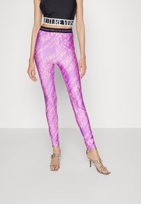 Lila leggings av glänsande, elastiskt material med ett upprepat textmönster. Bärs med en svart crop top och silverfärgade högklackade sandaler.