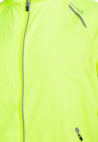 Veste légère jaune néon avec fermeture éclair intégrale, accents réfléchissants et texture lisse. Présente un logo de la marque sur l'épaule et la capuche.