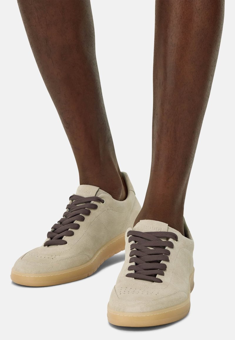 Beige suede sneakers with brown laces, rounded toe, and textured rubber sole, displaying a simple design and minimal branding.