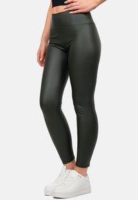 Leggings high-waisted di colore verde scuro, realizzati in un materiale elastico e lucido. Texture liscia senza cuciture visibili, abbinati a scarpe da ginnastica bianche.